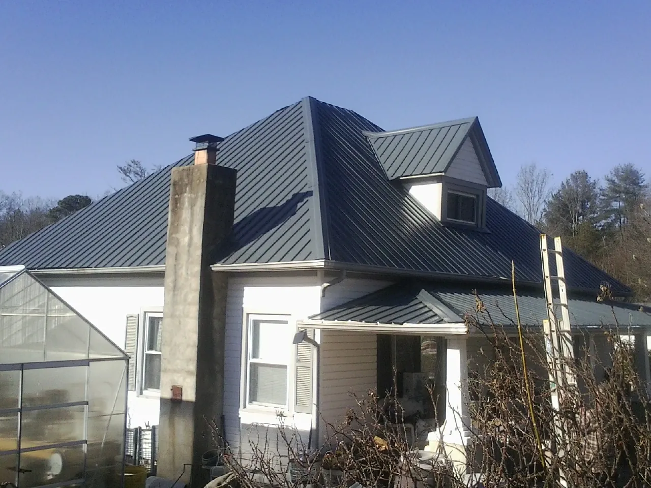 Dark blue standing seam metal roof on a white farmhouse with dormer — Slate & Tile Roof Repair by Roofing Brothers in Orchard